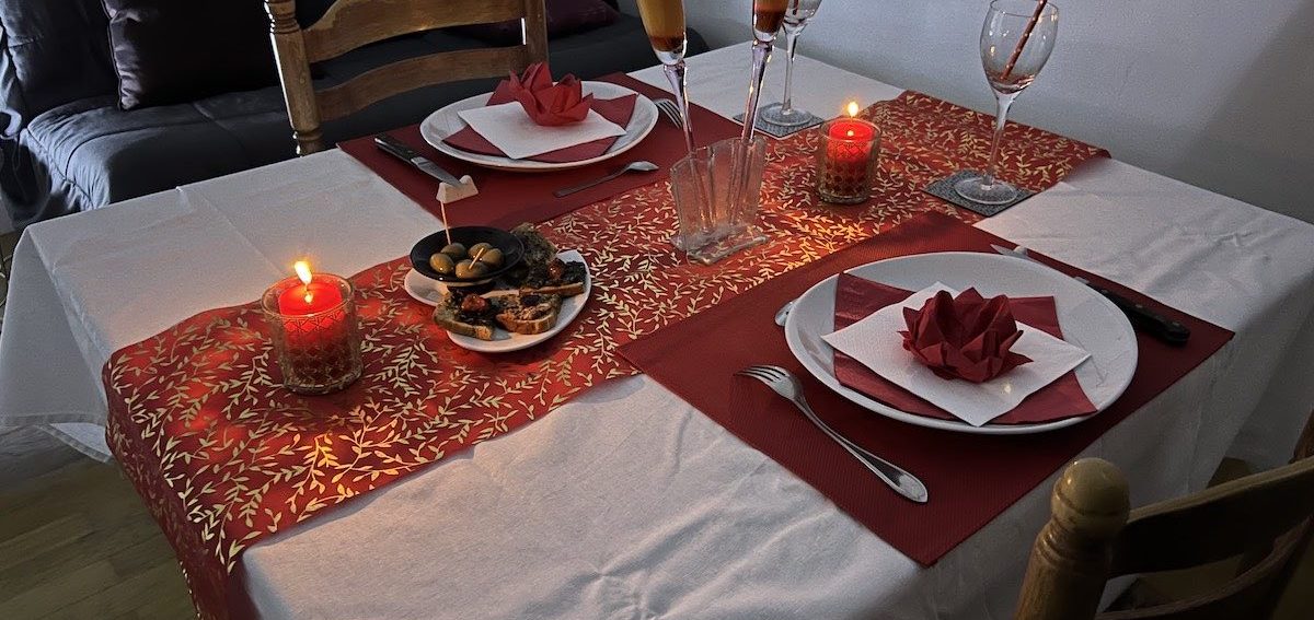 La table du dîner romantique aux chandelles dressée en rouge et blanc, bougies et fleurs en papier 