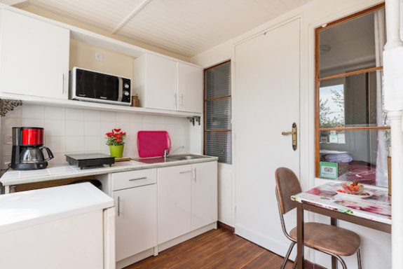 La cuisine blanche, simple et lumineuse de Goélette, équipée pour des repas rapides ou pique-nique avec table et 2 chaises