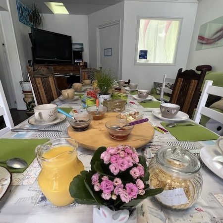 Table du petit déjeuner pour 8 convives dressée, confitures maison, fleurs et jus d'orange