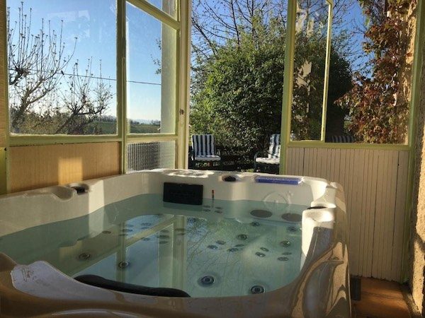 Jacuzzi 2 places ouvert sur la nature dans sa véranda intimiste, un espace bien-être et ressourcement. 