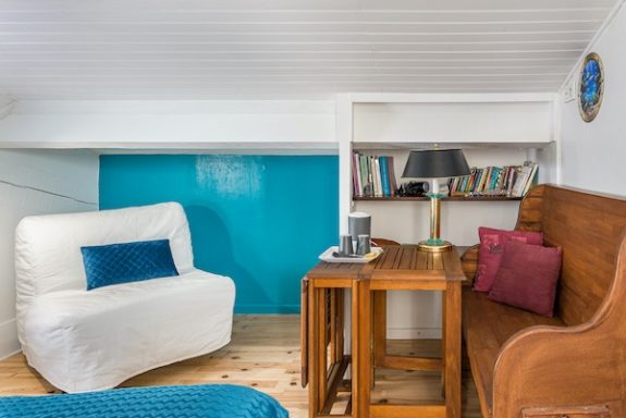 Vue sur le canapé BZ et sa table de détente, banc 2 places, étagères avec livres dans la chambre Goélette à L'Escale du Loup Blanc