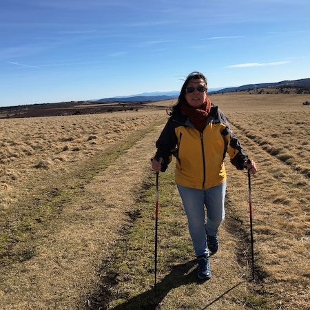 Personne marchant avec des bâtons de marche nordique dans des étendues herbeuses à perte de vue sous un grand ciel bleu.