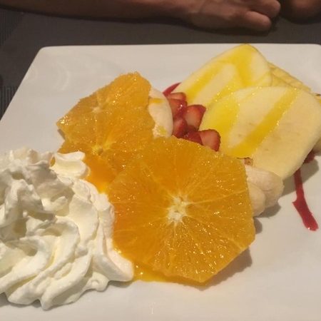 Dessert de tranches fines d'orange, de fraises, de poires et demi banane sur assiette blanche avec fleur de chantilly. 